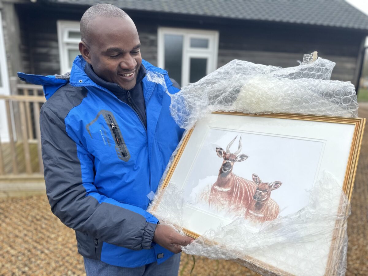 Dr Robert Aruho holding a painting of mountain bongo by Annabel Pope