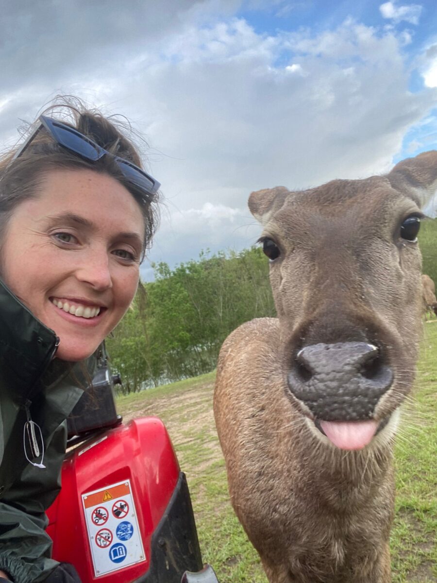 A white female smiling aith a sambar deer appearing to smile next to her