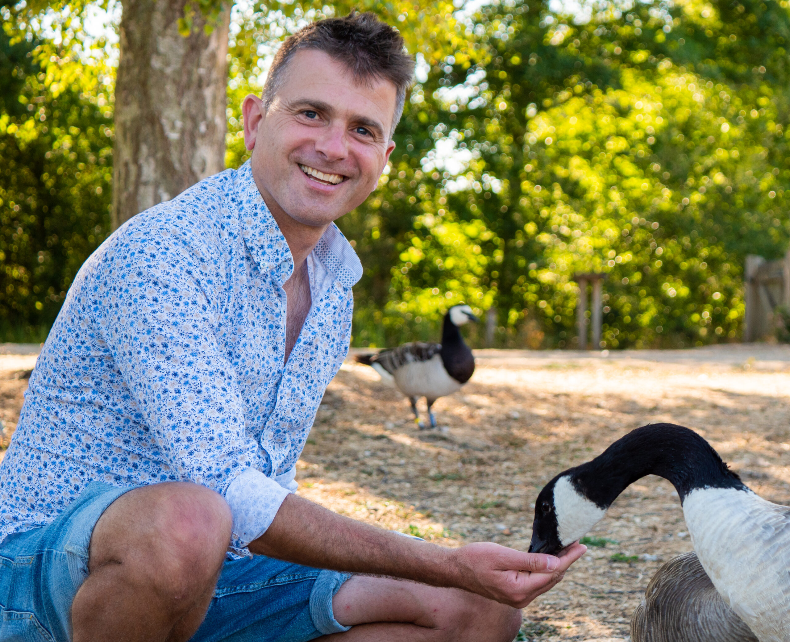 A caucasian male smiling and feeding a Canada goose
