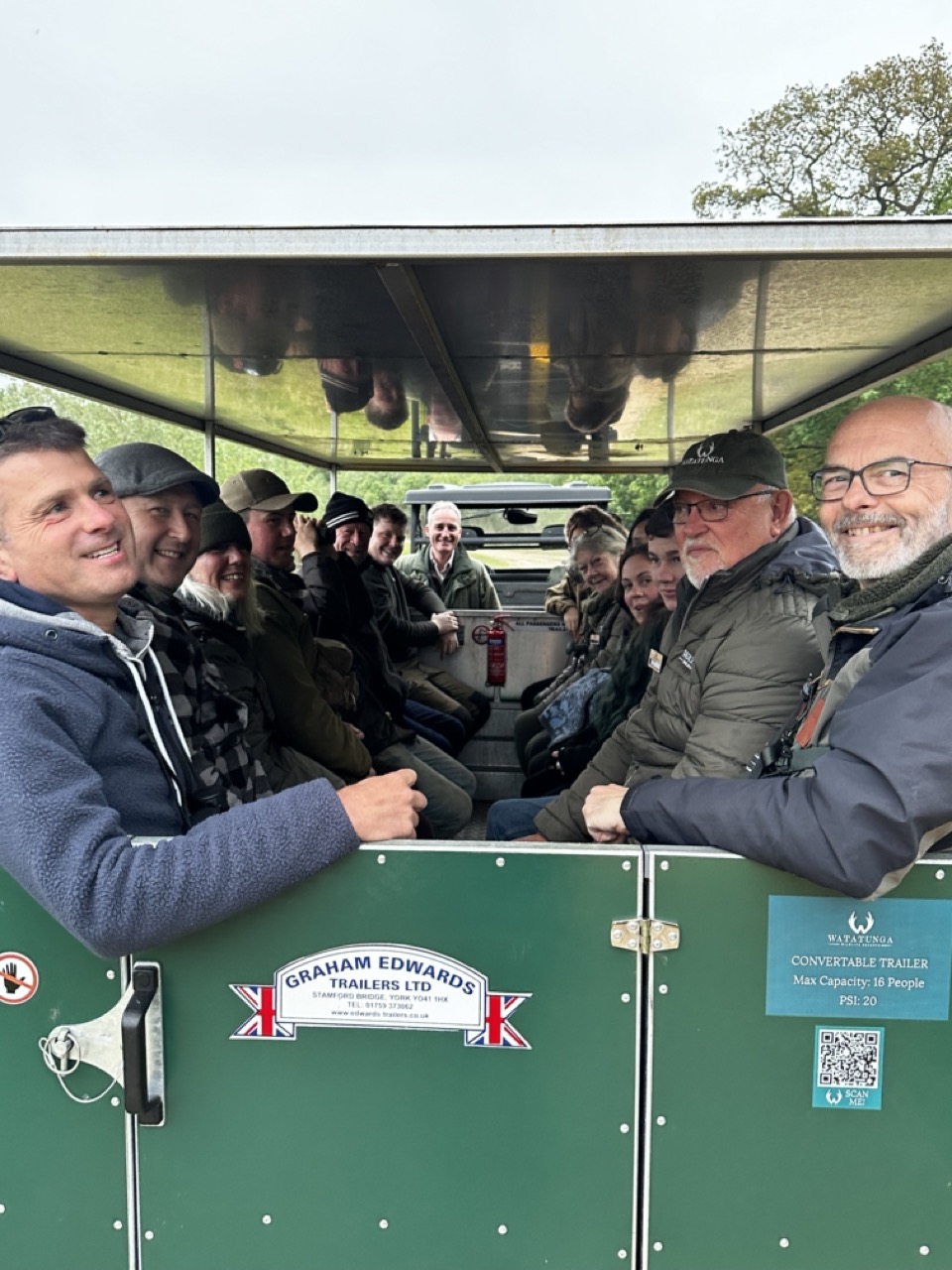 A green trailer with open sides filled with smiling people