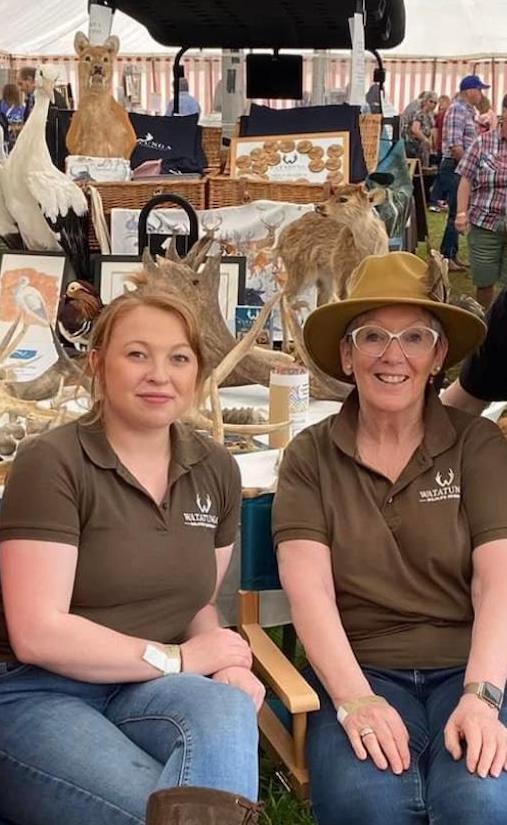 Two white women sitting at an educational stand about deer and antelope at a country fair