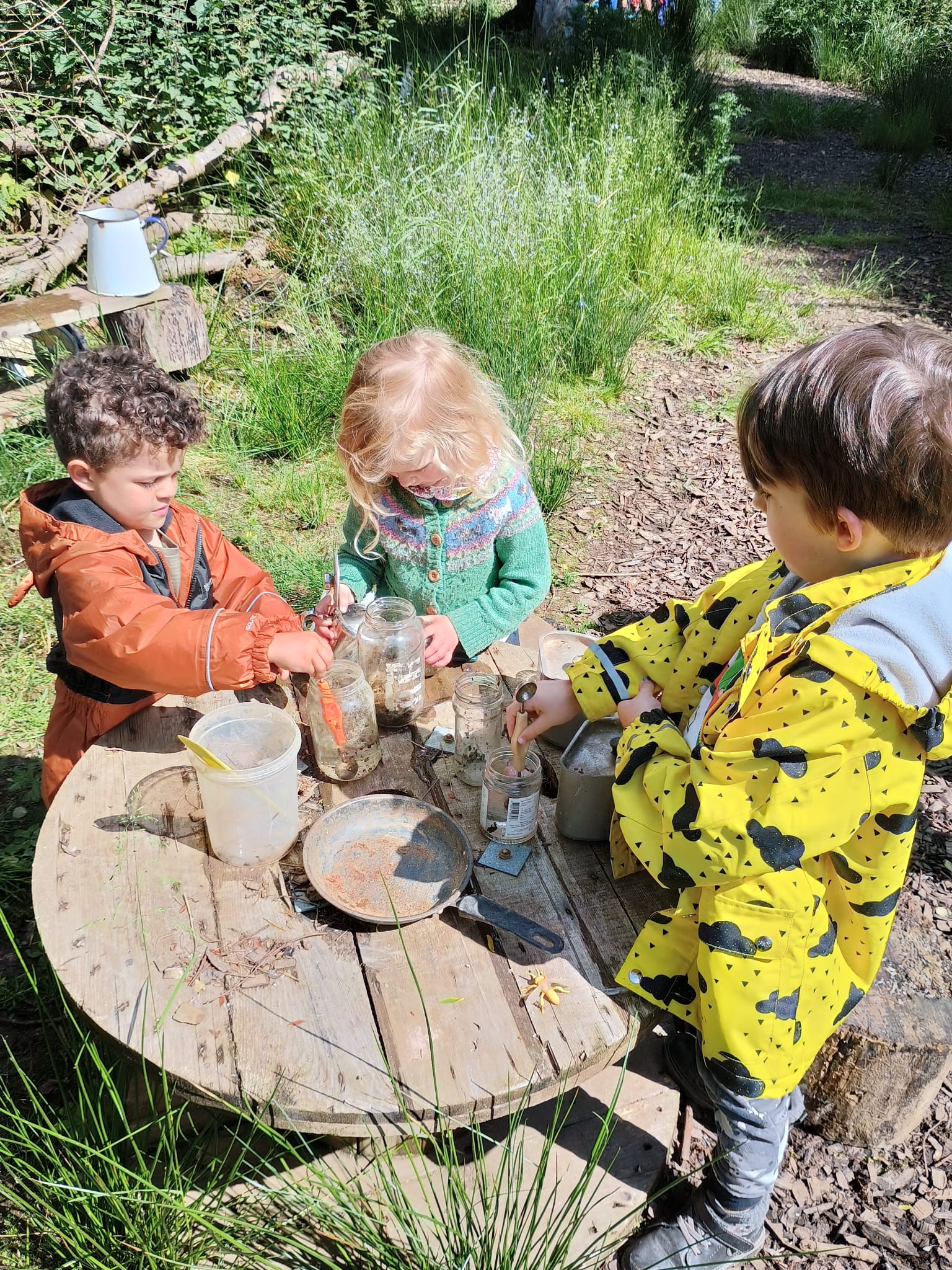 three children around a wooden table learning outside